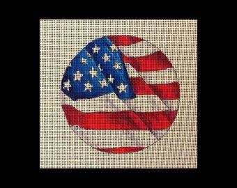 May include: A round needlepoint design featuring the American flag. The design includes a blue field with white stars and red and white stripes. The needlepoint is on a beige canvas.