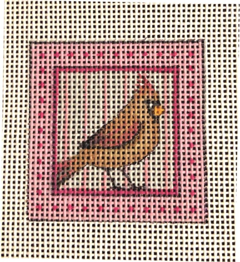 May include: Needlepoint canvas featuring a detailed bird design. The bird is depicted in shades of brown, yellow, and orange, set against a pink square border with a dotted pattern. The background is a white canvas with a grid pattern.