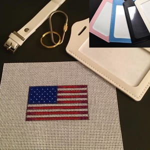 May include: An assortment of items including a white leather key fob, a gold-colored key ring, and a needlepoint canvas featuring the American flag. Also shown are several ID badge holders in pink, blue, black, and white.