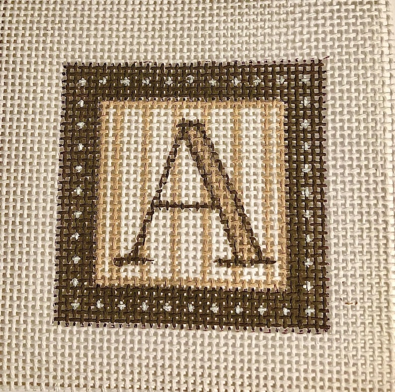May include: Square needlepoint canvas featuring the letter "A" in a brown, tan, and white color scheme. The letter is centered within a tan and brown border, with a brown outer border. The background is a neutral, off-white color.