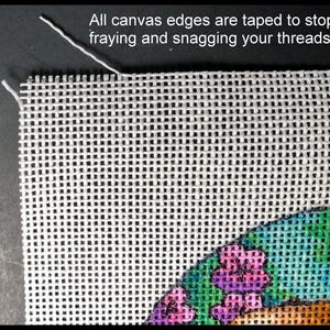 May include: Close-up of a white canvas with a grid pattern, with the text "All canvas edges are taped to stop fraying and snagging your threads." The canvas has colorful embroidery in the corner, featuring purple and green floral designs.