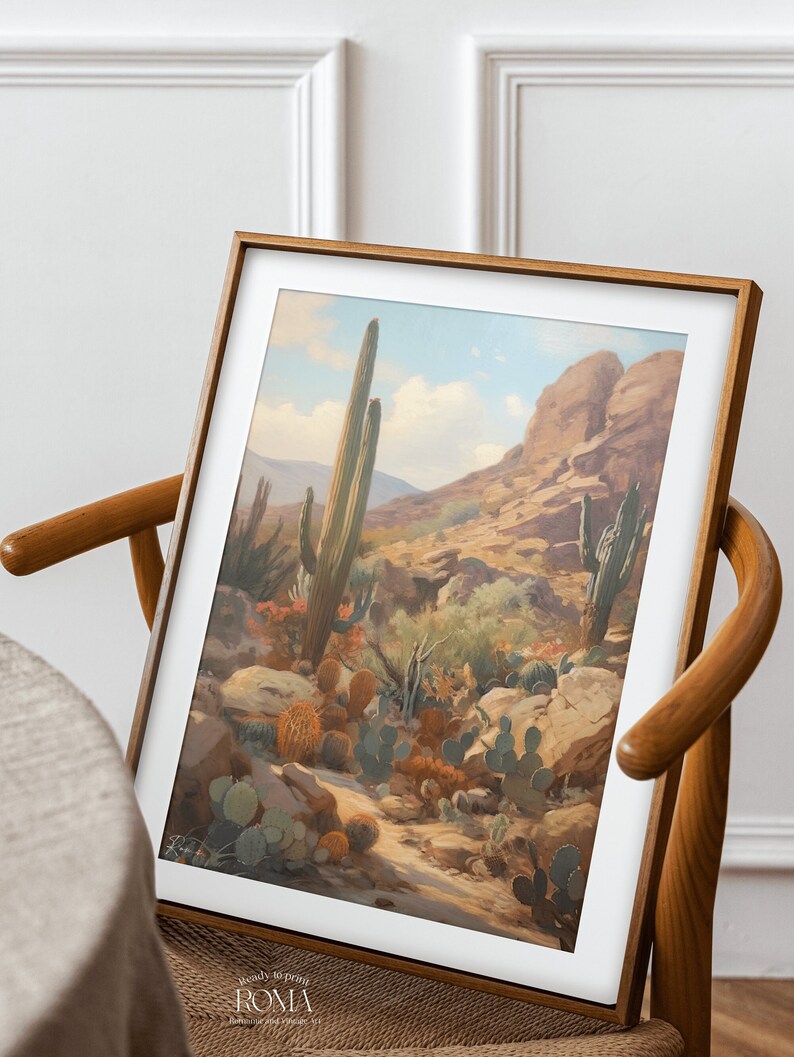 May include: A framed print of a desert landscape with tall cacti and smaller cacti in the foreground. The print is in a wooden frame and is hanging on a wall.