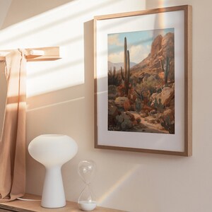 May include: A framed print of a desert landscape with tall cacti and a rocky mountain in the background. The print is in a light wood frame and is hanging on a light beige wall. The print is titled "Ready to Print Roma" and has the text "Romantic and Vintage Art" below the title.