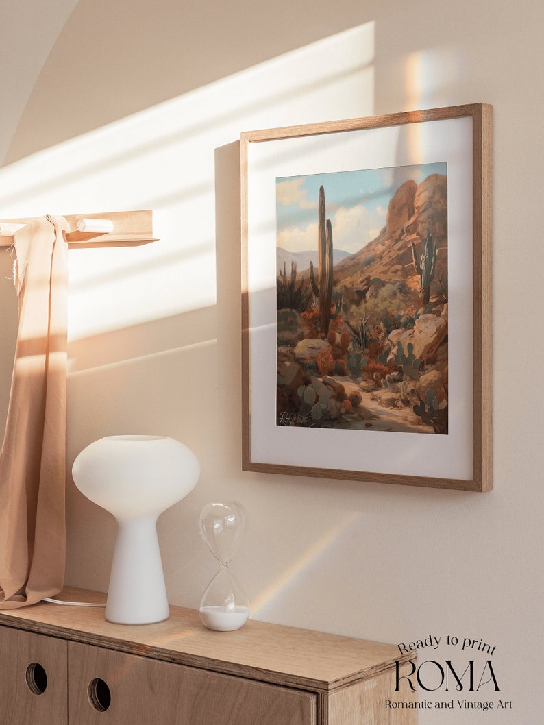 May include: A framed print of a desert landscape with tall cacti and a rocky mountain in the background. The print is in a light wood frame and is hanging on a light beige wall. The print is titled "Ready to Print Roma" and has the text "Romantic and Vintage Art" below the title.
