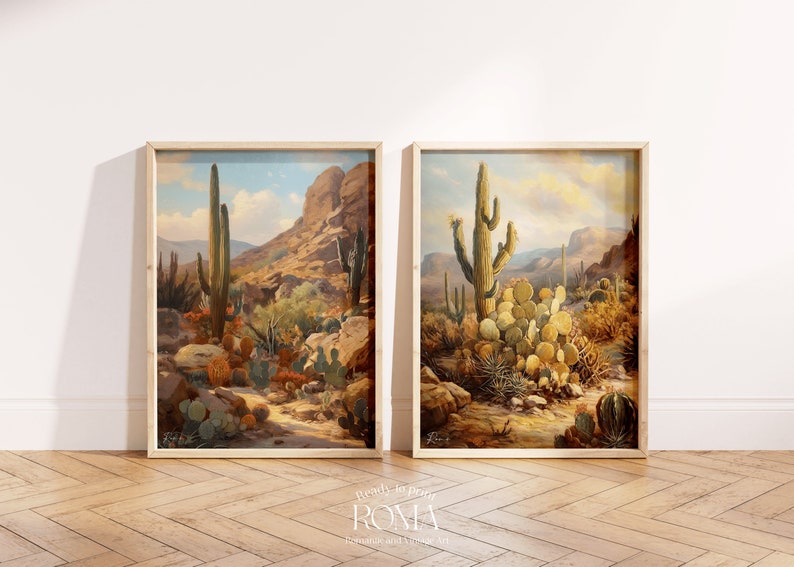 May include: Two framed paintings of desert landscapes with cacti and mountains. The paintings are in a light wood frame and are hanging on a white wall.