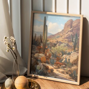 May include: A framed print of a desert landscape with cacti and a rocky mountain in the background. The sky is blue with white clouds. The print is in a light wood frame.