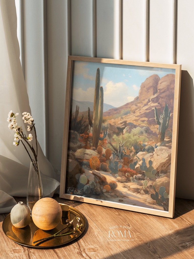 May include: A framed print of a desert landscape with cacti and a rocky mountain in the background. The sky is blue with white clouds. The print is in a light wood frame.