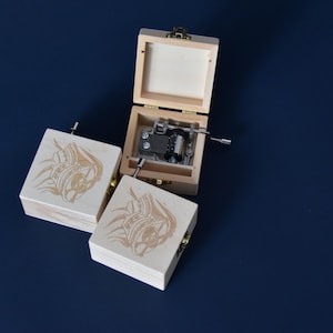 Può includere: Tre carillon in legno con disegni intricati sui coperchi. Le scatole sono chiuse, ma una è aperta, rivelando un meccanismo musicale argentato.