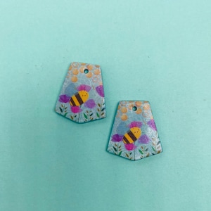 May include: Two blue and gold bee-themed charms with a bee and flowers on each. The charms have a hole at the top for hanging.