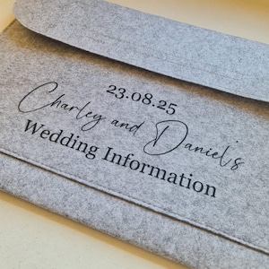 May include: Grey felt folder with the text "Charley and Daniel's Wedding Information" and the date "23.08.25" printed in black.