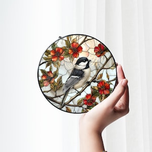 Puede incluir: Un panel redondo de vidrio emplomado con un p&aacute;jaro blanco y negro posado en una rama con flores rojas. El p&aacute;jaro est&aacute; rodeado de un fondo blanco con un sutil brillo iridiscente.