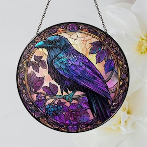 May include: A round stained glass window featuring a raven perched on a branch with purple leaves and berries. The raven has blue and purple feathers, a blue beak, and is set against a warm, light-colored background. The window is framed with a decorative border and a hanging chain.