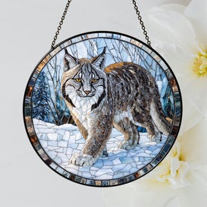 Peut inclure: Une fenêtre en verre teinté suspendu présente une image en mosaïque d'un lynx marchant dans une scène de forêt enneigée. Le lynx est brun et gris avec une poitrine blanche et un nez noir. La forêt est bleue et verte avec de la neige blanche au sol.