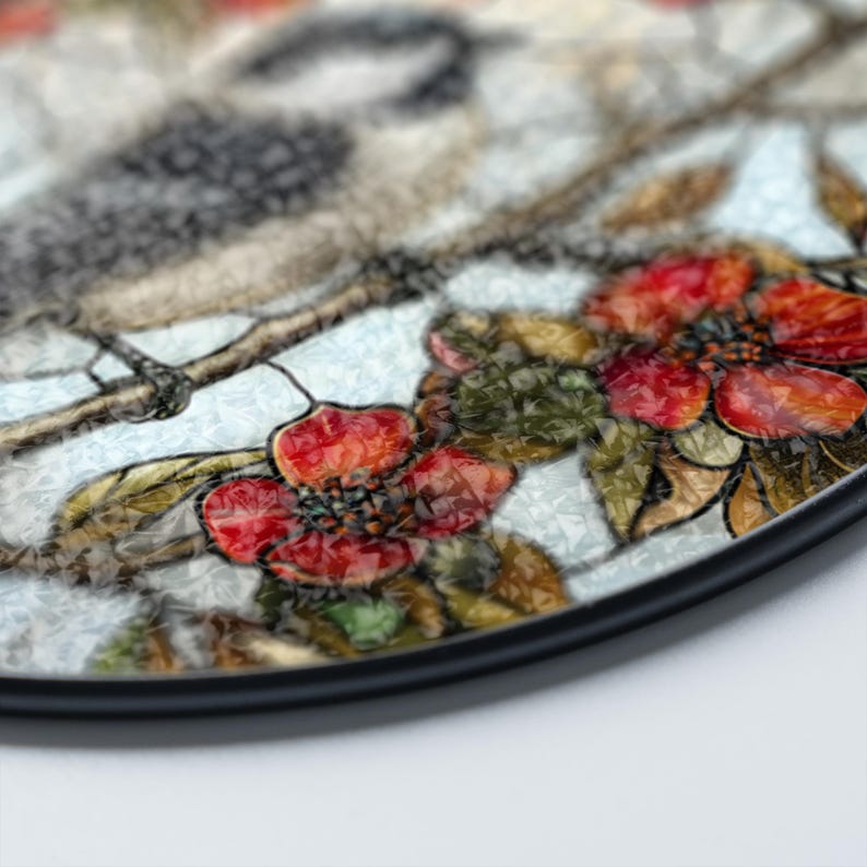 Puede incluir: Un plato redondo con borde negro, que presenta un dise&ntilde;o de vitral de un p&aacute;jaro posado en una rama con flores rojas. El fondo es azul claro con un patr&oacute;n blanco texturizado.