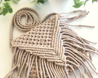 May include: A beige crocheted crossbody bag with a triangular shape and fringe details. The bag has a long strap and is made of a thick, textured yarn.