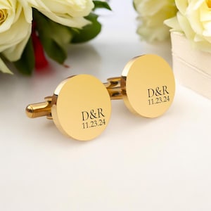 May include: Gold cufflinks with a round design. The cufflinks are engraved with the initials "D&R" and the date "11.23.24".