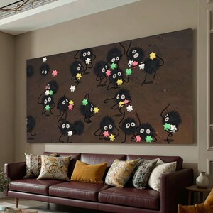 May include: A large rectangular canvas print featuring cartoon-like black creatures with star-shaped objects. The creatures have large eyes and are set against a brown background. The print hangs above a brown leather sofa with decorative pillows.