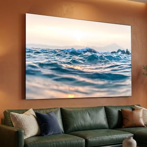 Puede incluir: Una gran impresión en lienzo enmarcada que representa olas del océano en primer plano. El agua es de un azul profundo, con toques dorados del sol poniente. El horizonte presenta una cordillera borrosa.