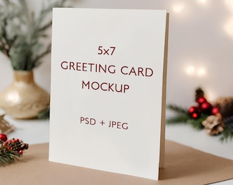 May include: A white 5x7 greeting card mockup with the text "5x7 Greeting Card Mockup PSD + JPEG" in red lettering. The card is standing upright on a brown surface with a vase and greenery in the background.