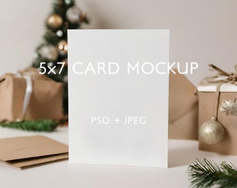 May include: A white 5x7 card mockup with the text "5x7 CARD MOCKUP" and "PSD + JPEG" on a white surface with brown gift boxes and a small Christmas tree in the background.
