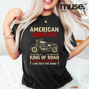 May include: A black short-sleeve t-shirt featuring a graphic of a motorcycle. The text reads AMERICAN CHOPPER, KING OF ROAD, SUPERIOR PERFORMANCE, and LIVE FAST DIE HARD. The design includes illustrations of spark plugs on the bottom sides.