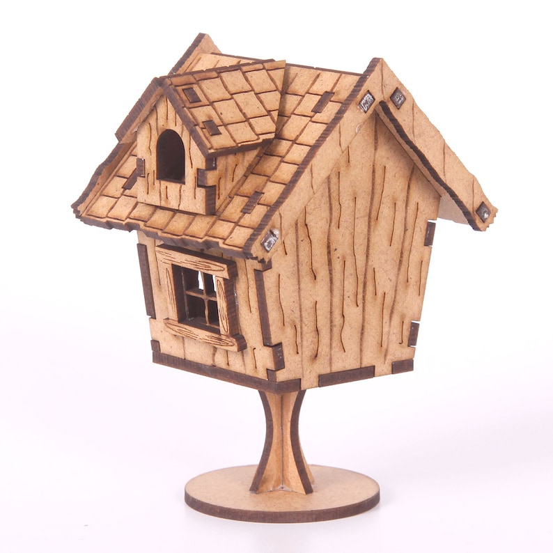 May include: A wooden model of a small house with a shingled roof, a window, and a door. The house is on a wooden stand.