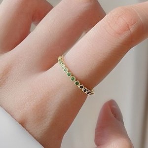 Könnte beinhalten: Ein goldener Ring mit einer Reihe kleiner grüner Edelsteine.