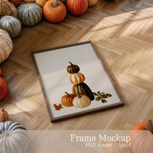 May include: A rectangular wooden frame containing a print of a stack of pumpkins. The artwork features a dark green pumpkin balanced on a light orange striped pumpkin, which sits atop a large dark green pumpkin, with two smaller pumpkins below.