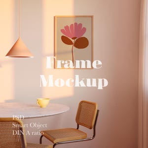Könnte beinhalten: Ein gerahmter Kunstdruck mit einer rosa Blume und einem braunen Stiel auf beigem Hintergrund. Die Worte "Frame Mockup" sind weiß. Die Szene umfasst einen runden Tisch, eine gelbe Tasse und einen Rattanstuhl. Das Bild ist in einem Raum.