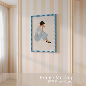 May include: A rectangular wall frame with a light blue beaded border containing an illustration of a person with dark hair sitting in a light blue patterned outfit. The frame is displayed on a wall with vertical beige and white stripes.
