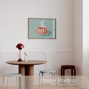 May include: A rectangular wooden frame containing a print of a red and white striped teacup on a saucer with steam rising, displayed on a wall above a round wooden table with a red lamp, two silver shakers, and three stools.