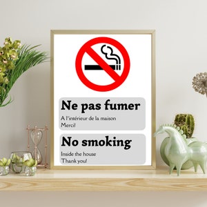 Puede incluir: Un cartel blanco con un círculo rojo y una línea diagonal que lo atraviesa. El círculo contiene un cigarrillo negro con humo saliendo de él. El cartel dice "Ne pas fumer" en francés y "No smoking" en inglés. También dice "A l'intérieur de la maison" en francés y "Inside the house" en inglés. El cartel termina con "Merci!" en francés y "Thank you!" en inglés.
