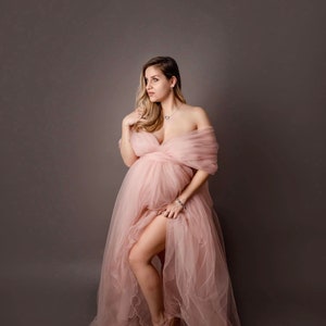 May include: A pregnant person in a pink tulle gown with a plunging neckline. The gown has a flowing skirt and the person is standing with one leg slightly raised.