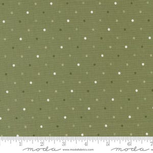 May include: Close-up of olive green fabric with a polka dot pattern. The dots are in shades of white, gray, and dark green. The fabric has a textured appearance and a ruler is at the bottom.