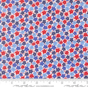 May include: A white fabric featuring a dense, repeating pattern of small five-petaled flowers in shades of bright red, light blue, and dark navy blue. A white ruler is visible at the bottom, showing a scale of 7 inches for the fabric width.