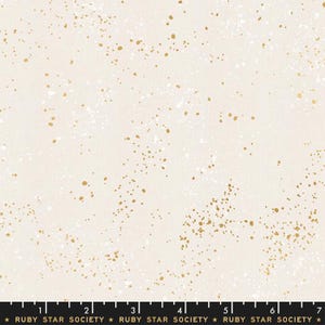 May include: Cream-colored fabric with a speckled pattern of white and gold dots. The fabric has a subtle texture and a light, airy feel. The bottom of the fabric has a ruler with the text "RUBY STAR SOCIETY".
