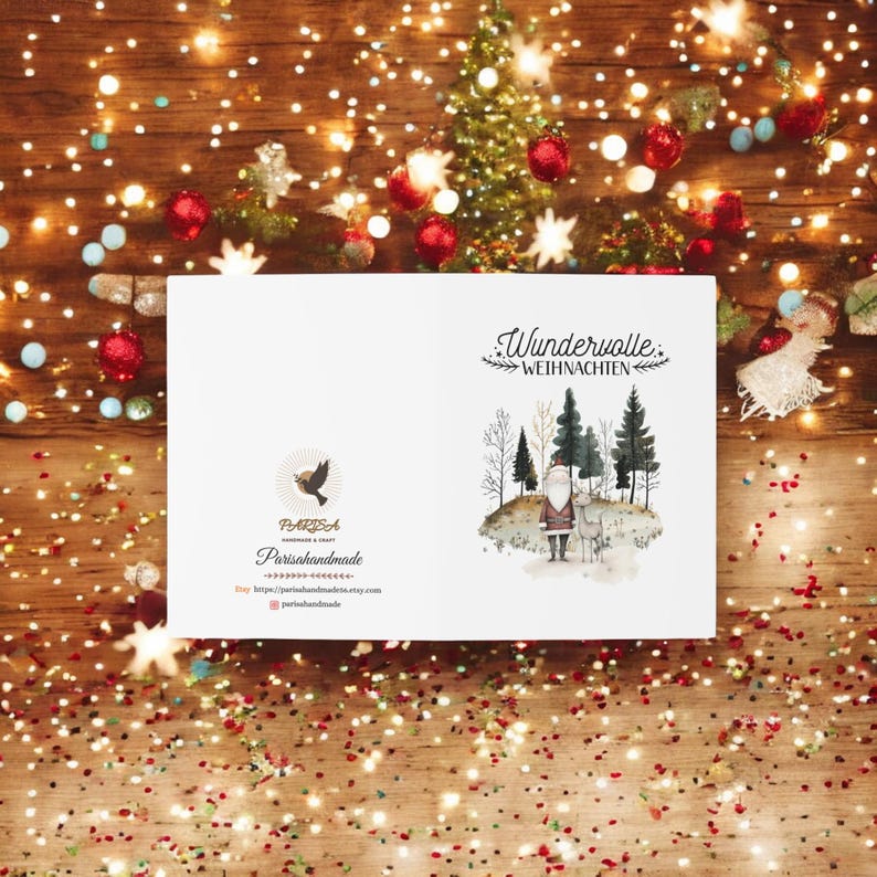May include: A white card with a watercolor illustration of a winter scene with a Santa Claus figure and a deer. The text "Wundervolle Weihnachten" is printed in black at the top of the card. The card also features a logo for "Parissahandmade" with a bird graphic and the website address.