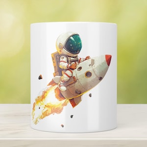 Könnte beinhalten: Ein weißer Keramikbecher mit einer farbenfrohen Grafik eines Astronauten im weißen Anzug, der auf einer grauen Rakete reitet. Die Rakete hat eine rote Spitze und stößt eine leuchtend orange-gelbe Flamme aus, umgeben von kleinen dunklen Gesteinsbrocken.