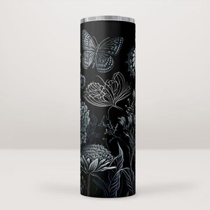 Puede incluir: Un vaso de acero inoxidable negro con un diseño floral y de mariposa blanco. El diseño presenta mariposas, flores y hojas.