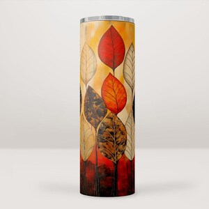 Pode incluir: Um copo de aço inoxidável com um design abstrato colorido de folhas em tons de vermelho, laranja, amarelo e marrom. As folhas estão dispostas verticalmente no copo.