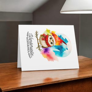 May include: A white card with a watercolor illustration of an owl wearing a Santa hat and scarf. The owl is perched on a branch in front of a colorful background. The text "Wundervolle Weihnachten" is printed on the card.