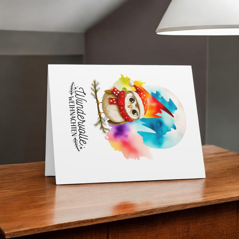 May include: A white card with a watercolor illustration of an owl wearing a Santa hat and scarf. The owl is perched on a branch in front of a colorful background. The text "Wundervolle Weihnachten" is printed on the card.