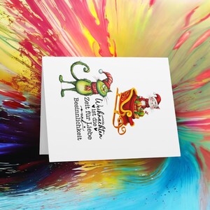 May include: A Christmas card with a green cat wearing a red Santa hat and a white cat riding in a red sleigh. The text on the card reads "Weihnachten ist die Zeit f&uuml;r Liebe und Besinnlichkeit".