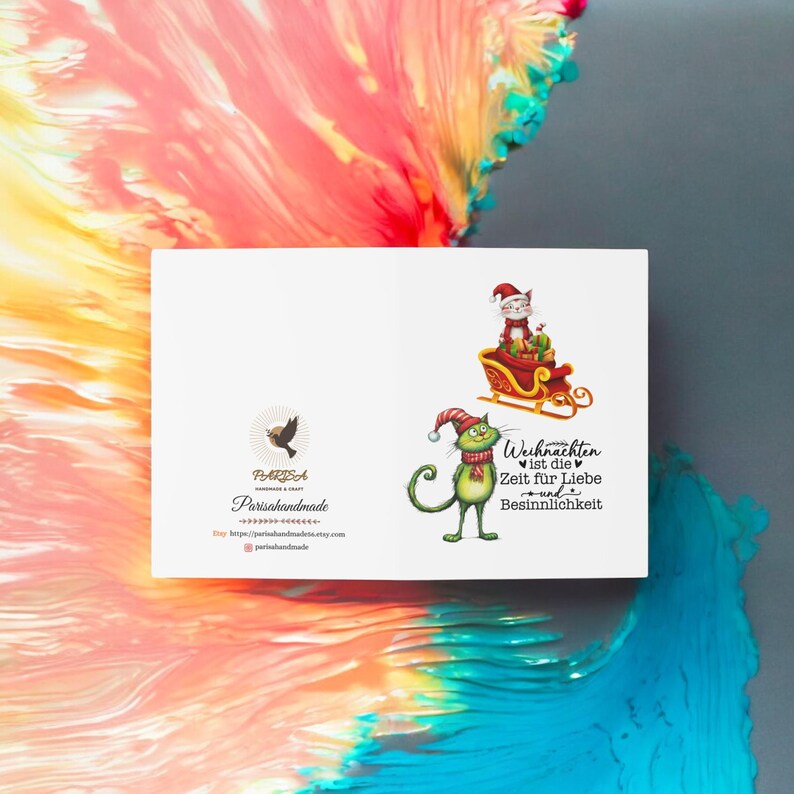 May include: A white card with a green cat wearing a red Santa hat and riding in a red sleigh pulled by a white cat wearing a Santa hat. The text on the card reads "Weihnachten ist die Zeit f&uuml;r Liebe und Besinnlichkeit".