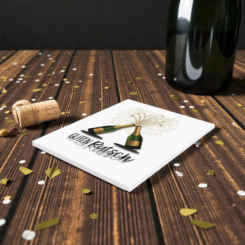May include: A white square coaster with a champagne bottle illustration and the text "Guten Rutsch" in black. A cork and confetti are scattered on a wooden surface. A green champagne bottle is in the background.