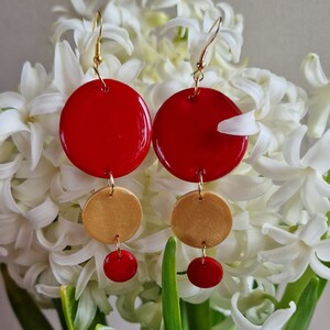 May include: Red and gold dangle earrings with three round shapes. The top shape is red, the middle shape is gold, and the bottom shape is red.