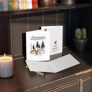 May include: A white card with a watercolor illustration of a Santa Claus figure in a forest setting. The text "Wundervolle Weihnachten" is written in black script on the front of the card.