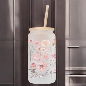 Könnte beinhalten: Eine mattierte Glaswasserflasche mit Bambusdeckel und Strohhalm. Die Flasche hat ein Blumenmuster mit rosa und weißen Blüten.