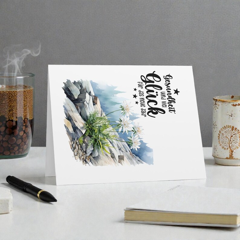 May include: A white greeting card with a watercolor illustration of a mountain scene with white flowers. The card has German text that reads "Gesundheit und viel Gl&uuml;ck f&uuml;r das neue Jahr."