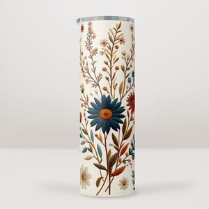 Pode incluir: Um copo branco com um padrão floral com flores azuis, vermelhas e marrons. As flores estão dispostas em um design semelhante a um buquê.